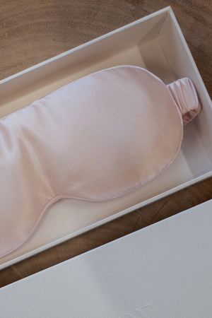 Pink heated silk eye mask in a white box on a wooden surface